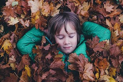 Kindermeditation: Kind genießt im Laub die Ruhe Kindermeditation: Kind genießt im Laub die Ruhe